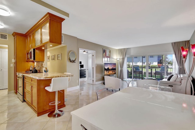 kitchen featuring ceiling fan, light tile patterned floors, stainless steel appliances, a breakfast bar, and light stone countertops