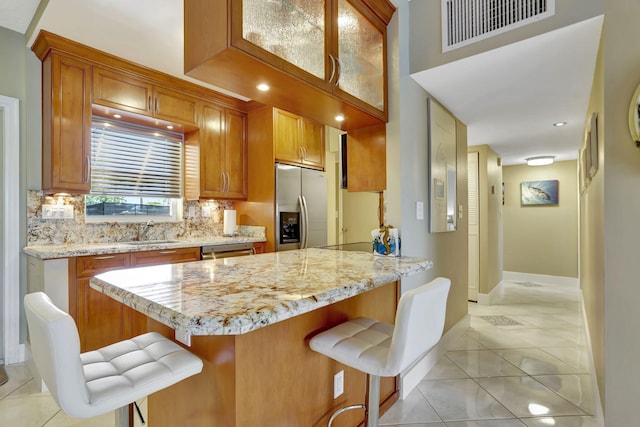 kitchen featuring kitchen peninsula, light tile patterned floors, appliances with stainless steel finishes, a kitchen breakfast bar, and decorative backsplash