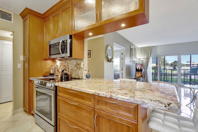 kitchen featuring light stone countertops, appliances with stainless steel finishes, light tile patterned floors, and decorative backsplash