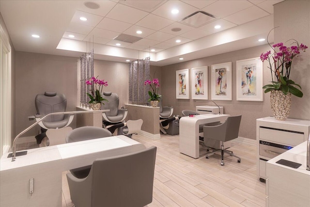 office space with light wood-type flooring, a tray ceiling, and a drop ceiling