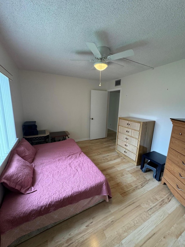 bedroom with ceiling fan, light hardwood / wood-style floors, and a textured ceiling