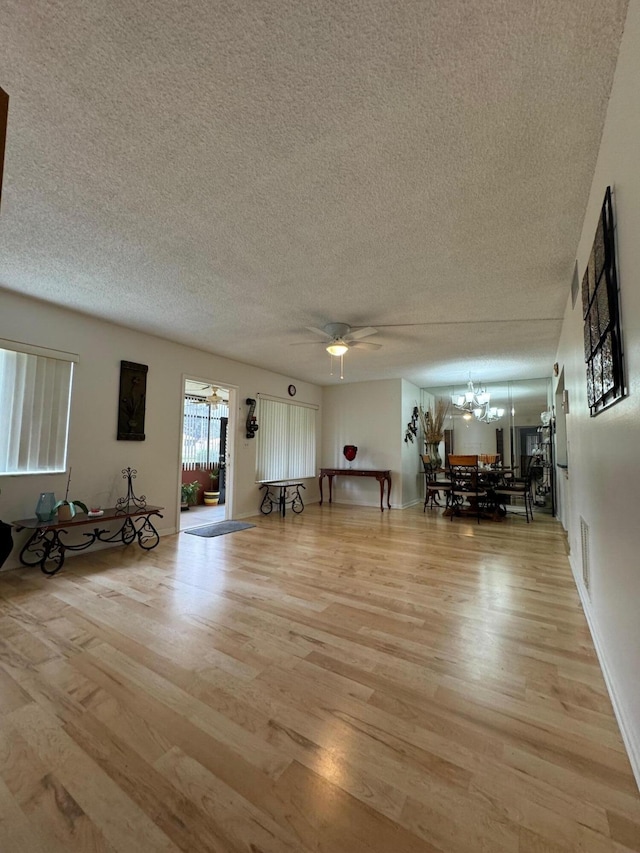 interior space with ceiling fan with notable chandelier, light wood-type flooring, and a textured ceiling