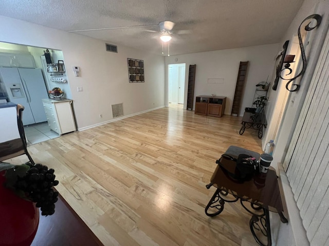 living room featuring ceiling fan, a textured ceiling, and light wood-type flooring