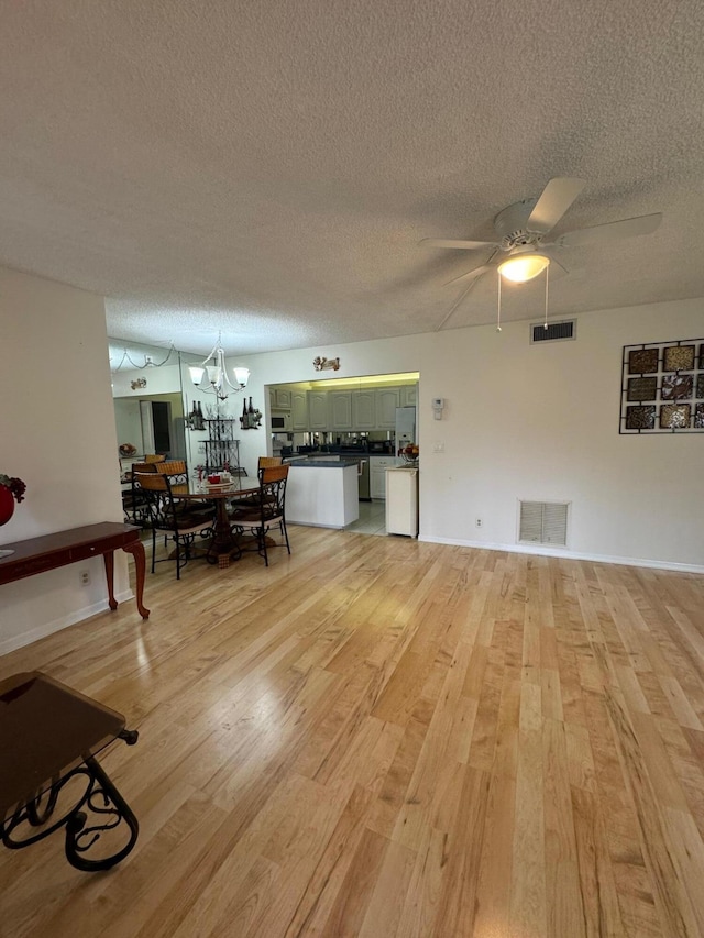 living room with ceiling fan with notable chandelier, light hardwood / wood-style flooring, and a textured ceiling