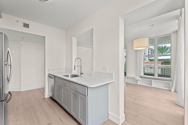 kitchen featuring appliances with stainless steel finishes, sink, light wood-type flooring, and gray cabinetry