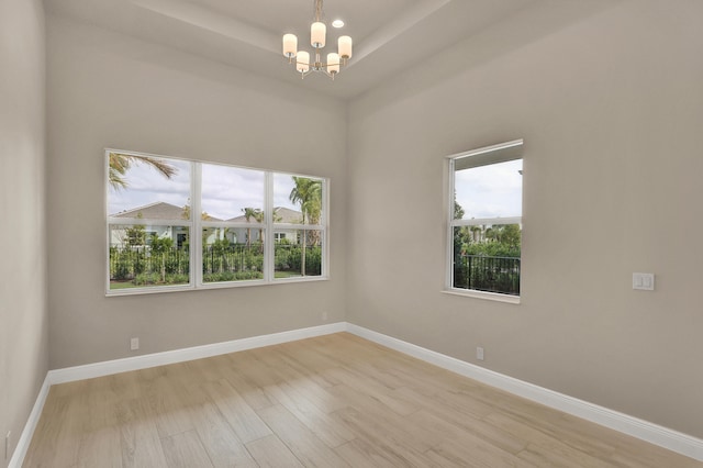 empty room with a chandelier, light hardwood / wood-style flooring, and a healthy amount of sunlight