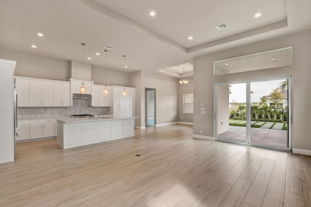 kitchen featuring hanging light fixtures, light hardwood / wood-style flooring, backsplash, an island with sink, and white cabinets