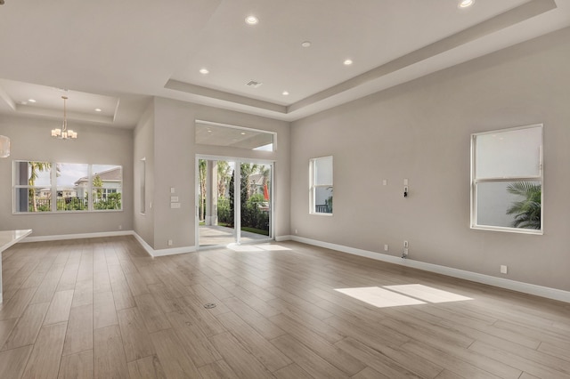 interior space with a towering ceiling, light wood-type flooring, a tray ceiling, and a notable chandelier