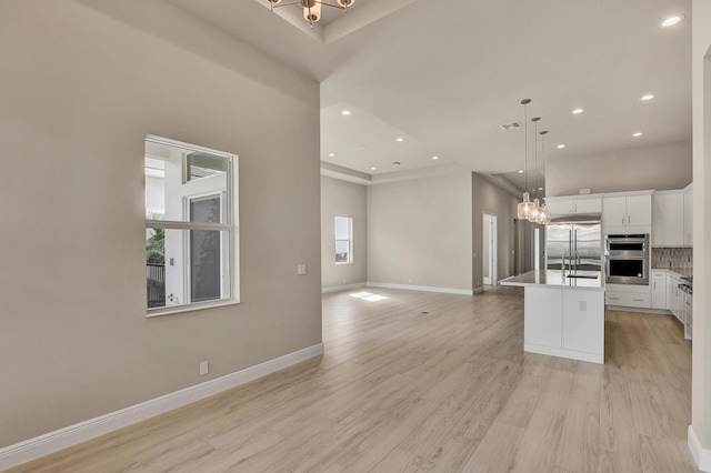 kitchen with white cabinetry, hanging light fixtures, light hardwood / wood-style flooring, a kitchen island with sink, and appliances with stainless steel finishes