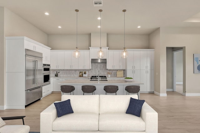 kitchen featuring white cabinets, a kitchen island with sink, hanging light fixtures, and appliances with stainless steel finishes