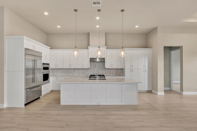 kitchen featuring stainless steel appliances, light hardwood / wood-style floors, decorative light fixtures, a kitchen island with sink, and white cabinets