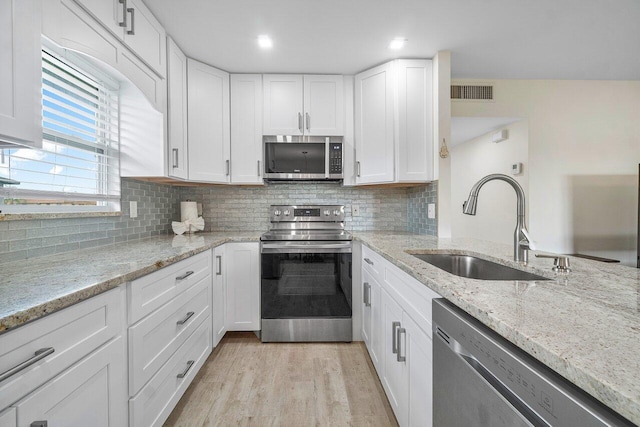 kitchen featuring stainless steel appliances, white cabinets, sink, light stone countertops, and light hardwood / wood-style flooring