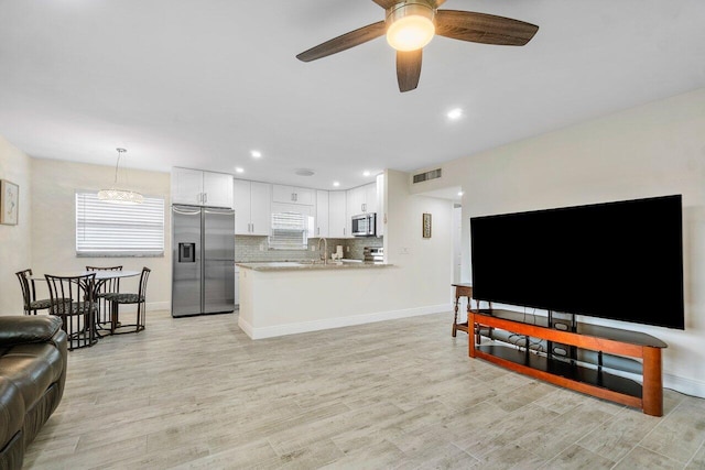 living room featuring ceiling fan with notable chandelier, sink, and light wood-type flooring