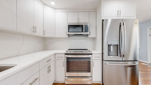 kitchen with tasteful backsplash, light hardwood / wood-style flooring, light stone countertops, appliances with stainless steel finishes, and white cabinets