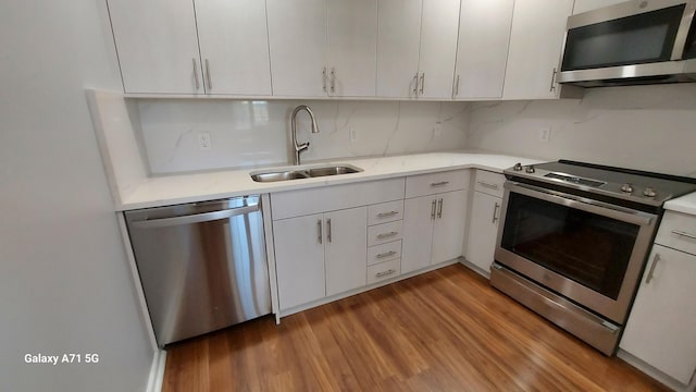 kitchen with appliances with stainless steel finishes, white cabinetry, dark hardwood / wood-style flooring, tasteful backsplash, and sink