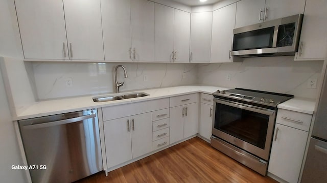 kitchen with hardwood / wood-style floors, white cabinets, stainless steel appliances, decorative backsplash, and sink