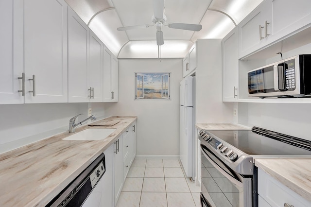 kitchen with appliances with stainless steel finishes, sink, light tile patterned floors, white cabinetry, and ceiling fan