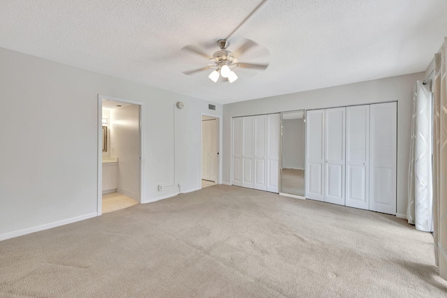 unfurnished bedroom featuring connected bathroom, light colored carpet, a textured ceiling, two closets, and ceiling fan