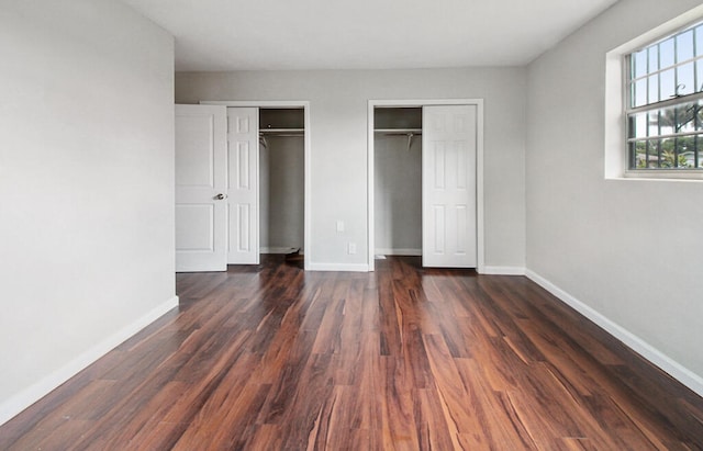 unfurnished bedroom featuring two closets and dark wood-type flooring