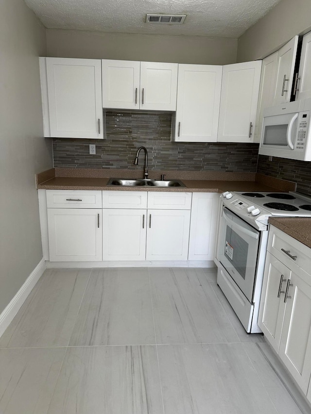 kitchen with light tile patterned flooring, tasteful backsplash, white cabinets, white appliances, and sink