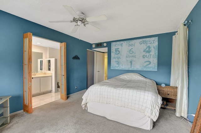 bedroom featuring ceiling fan, a textured ceiling, ensuite bath, and light carpet