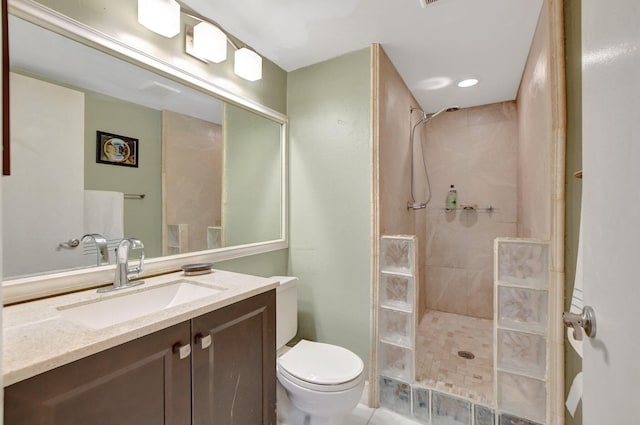 bathroom with toilet, a tile shower, vanity, and tile patterned floors