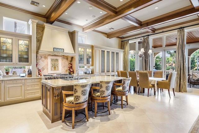 kitchen featuring premium range hood, a center island with sink, cream cabinetry, a kitchen breakfast bar, and light stone countertops