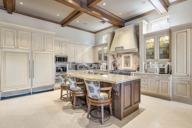 kitchen with cream cabinets, a center island with sink, and custom range hood