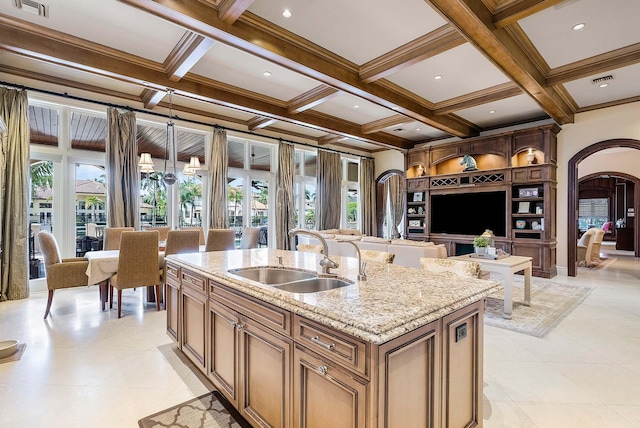 kitchen featuring coffered ceiling, a center island with sink, sink, and a healthy amount of sunlight