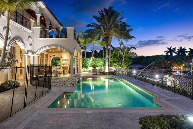 pool at dusk with ceiling fan and a patio area