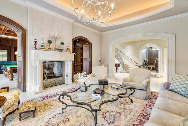 living room with a notable chandelier, a tray ceiling, a tiled fireplace, and ornamental molding