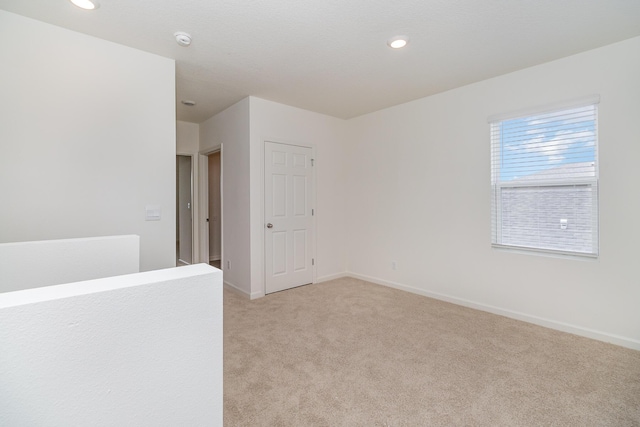 spare room with baseboards, recessed lighting, and light carpet