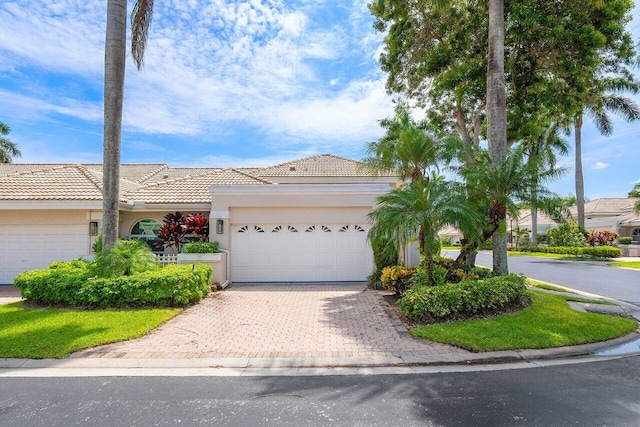 ranch-style home featuring an attached garage, a tiled roof, decorative driveway, and stucco siding