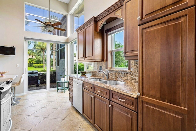 kitchen with light tile patterned floors, dishwasher, light stone counters, backsplash, and a sink