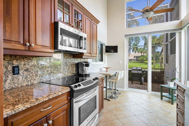 kitchen featuring tasteful backsplash, stone countertops, light tile patterned floors, a towering ceiling, and stainless steel appliances