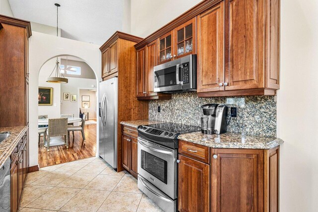 kitchen with decorative light fixtures, decorative backsplash, light tile patterned floors, light stone counters, and stainless steel appliances