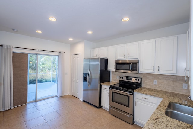 kitchen with sink, stainless steel appliances, light stone counters, decorative backsplash, and white cabinets