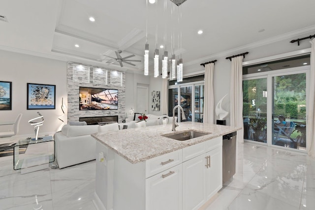 kitchen with sink, white cabinetry, hanging light fixtures, a large fireplace, and a center island with sink