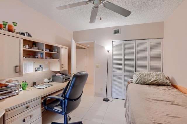 bedroom with built in study area, visible vents, light tile patterned flooring, a closet, and a textured ceiling