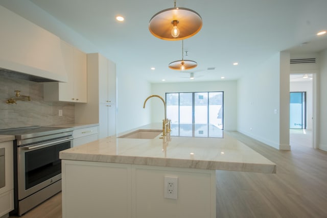 kitchen featuring a kitchen island with sink, electric stove, hanging light fixtures, white cabinets, and sink