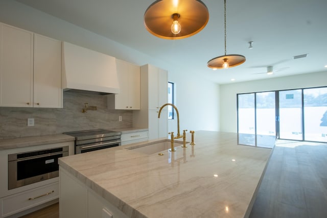 kitchen featuring custom exhaust hood, hanging light fixtures, stainless steel stove, white cabinets, and sink