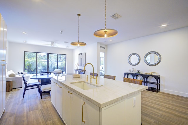 kitchen with sink, decorative light fixtures, white cabinets, and a center island with sink