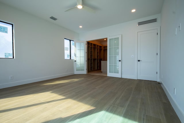 unfurnished bedroom featuring french doors, a closet, multiple windows, a walk in closet, and ceiling fan