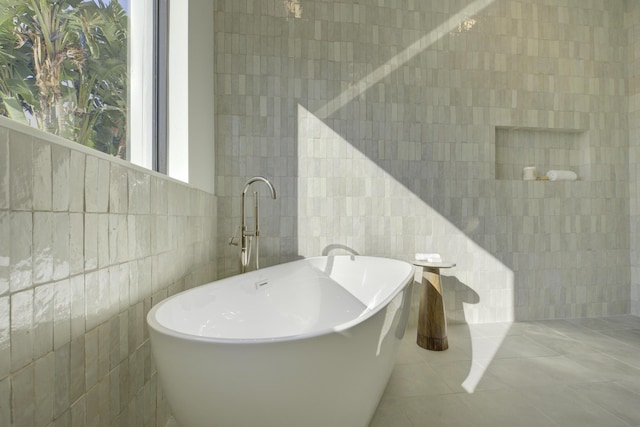 bathroom with a washtub, tile patterned flooring, and tile walls