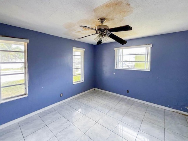 empty room featuring a textured ceiling, light tile patterned floors, a ceiling fan, and baseboards