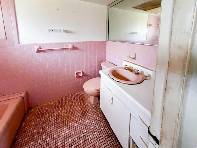 bathroom with tile walls, a wainscoted wall, vanity, and toilet