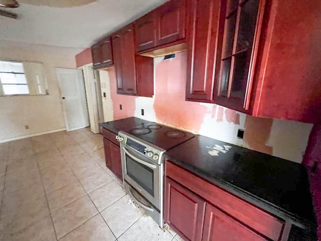 kitchen with stainless steel electric range oven, light tile patterned floors, dark countertops, dark brown cabinets, and baseboards