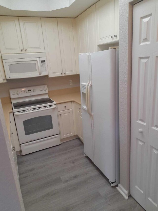 kitchen with white cabinetry, wood-type flooring, and white appliances