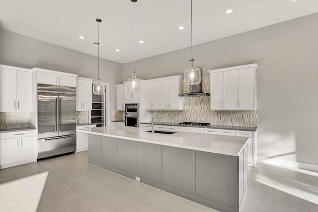 kitchen with pendant lighting, sink, a large island with sink, stainless steel appliances, and wall chimney range hood