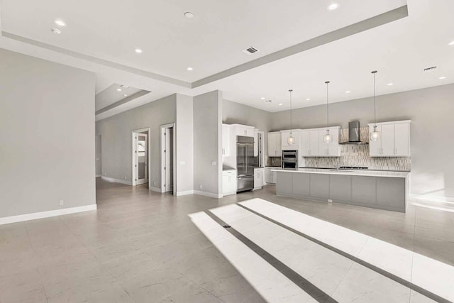 kitchen with pendant lighting, appliances with stainless steel finishes, white cabinetry, wall chimney exhaust hood, and a large island with sink